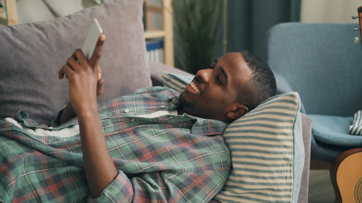 Mann liegt entspannt auf dem Sofa und schaut auf sein Smartphone