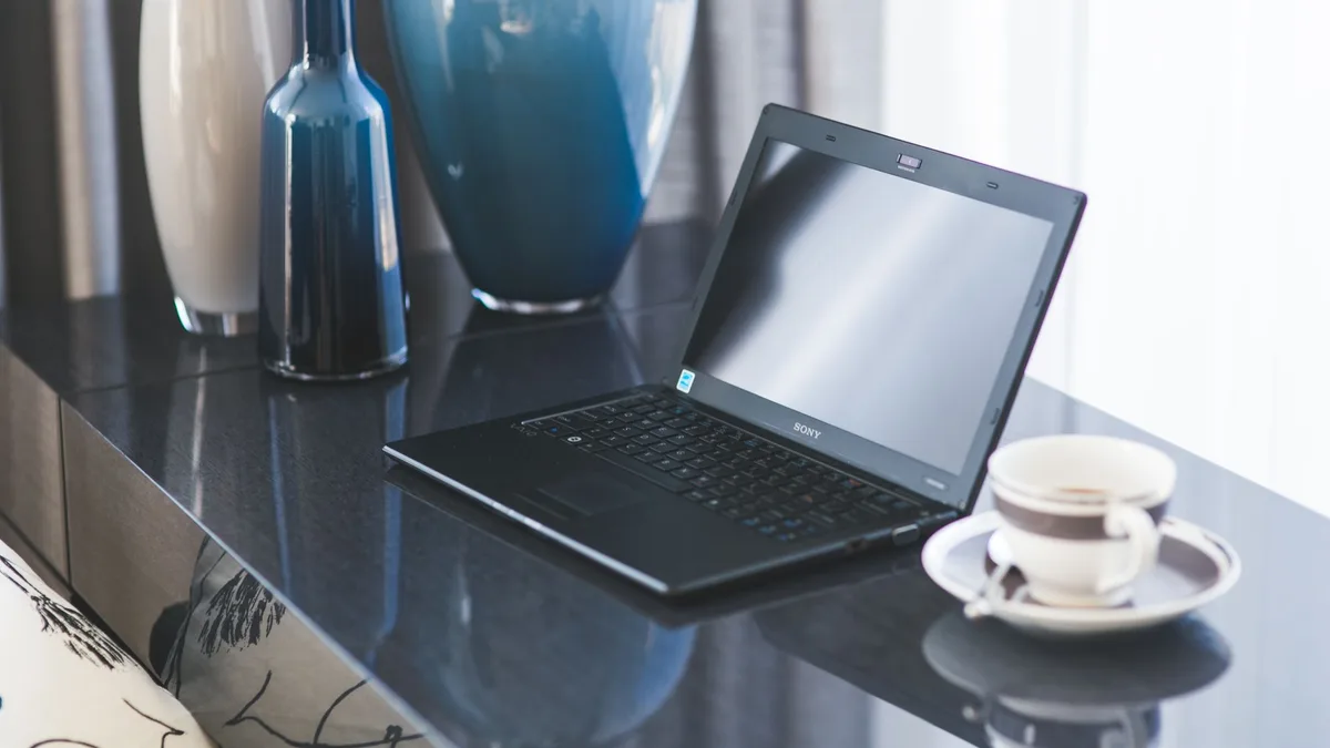 Laptop auf einem Glastisch neben einer Kaffeetasse und dekorativen Vasen