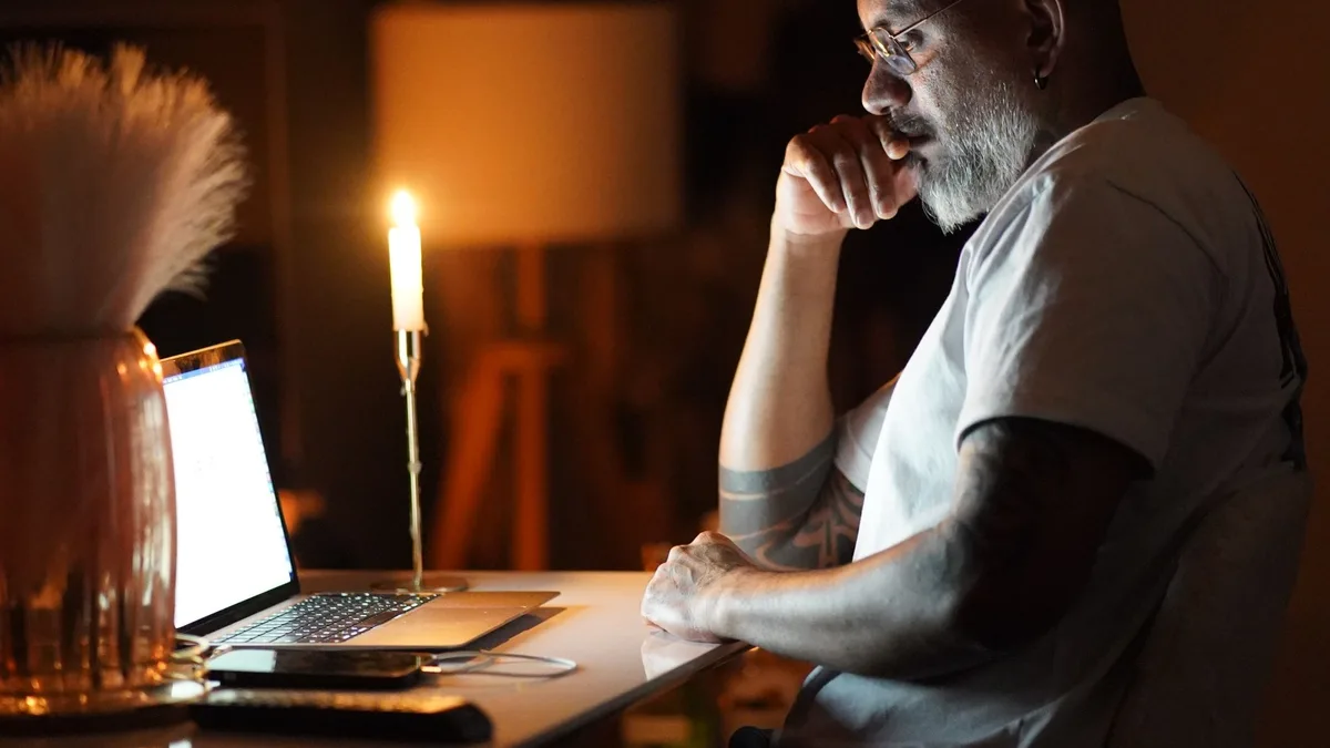Mann sitzt abends bei Kerzenlicht konzentriert vor seinem Laptop