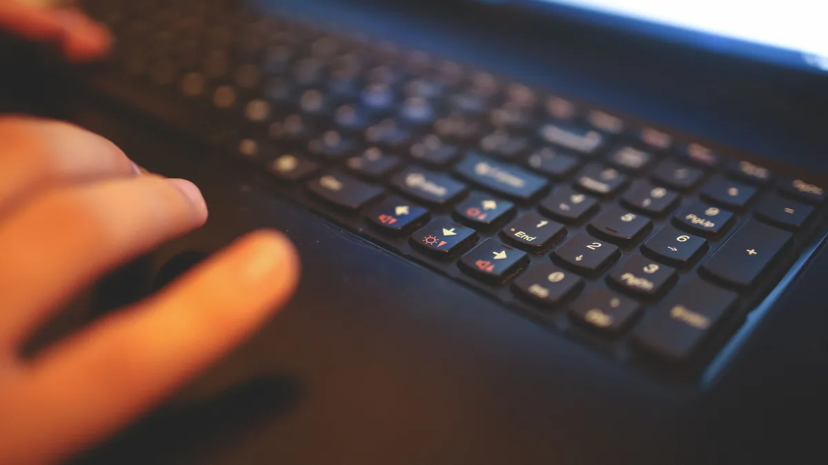 Nahaufnahme von Fingern auf einer dunklen Laptop-Tastatur, im Hintergrund ein helles, unscharfes Display