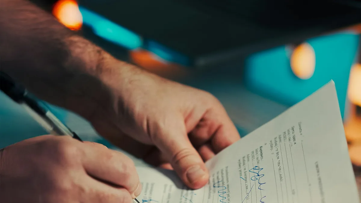 Nahaufnahme einer Hand, die einen Vertrag auf Papier unterschreibt