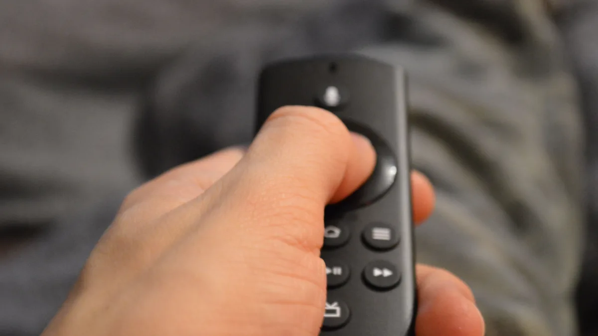 Hand hält eine schwarze Streaming-Fernbedienung mit rotem Knopf