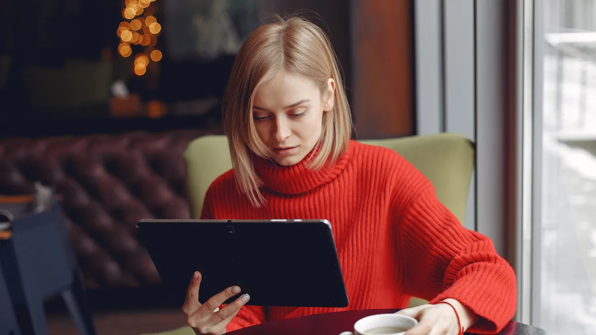 Frau sitzt nachdenklich in einem Café und blickt auf ein Tablet mit ausgeschaltetem Display