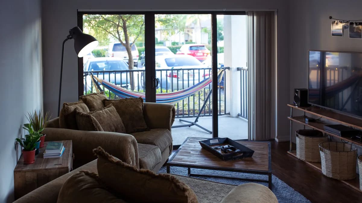 Minimalistisches, helles Wohnzimmer mit ausgeschaltetem Flachbildfernseher und Sitzecke am Fenster