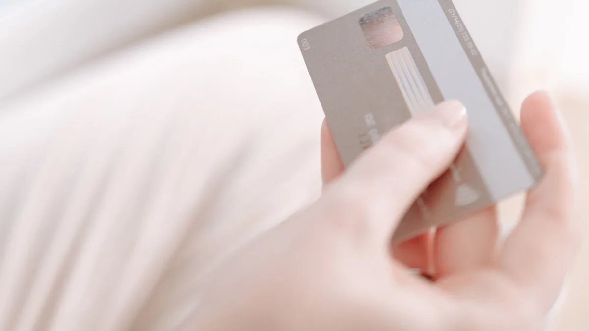 Person hält ein Smartphone mit unscharfer App-Ansicht und eine Zahlungskarte in der Hand