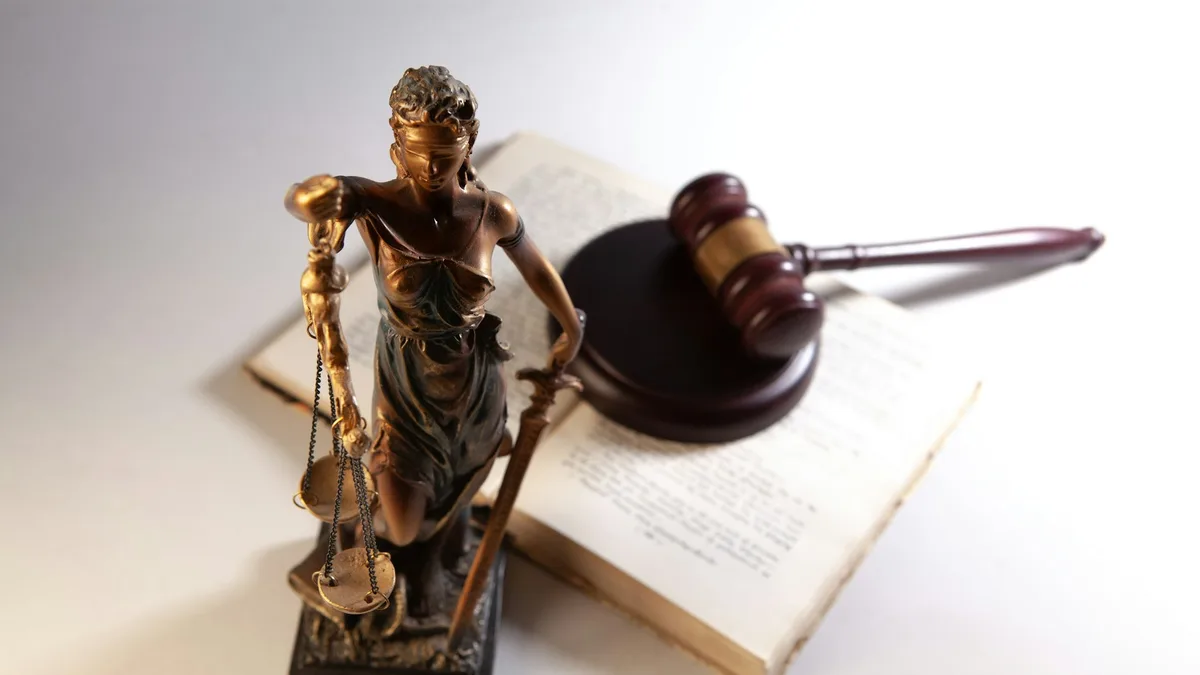 Justitia-Figur mit Waage neben einem Richterhammer und einem aufgeschlagenen Buch