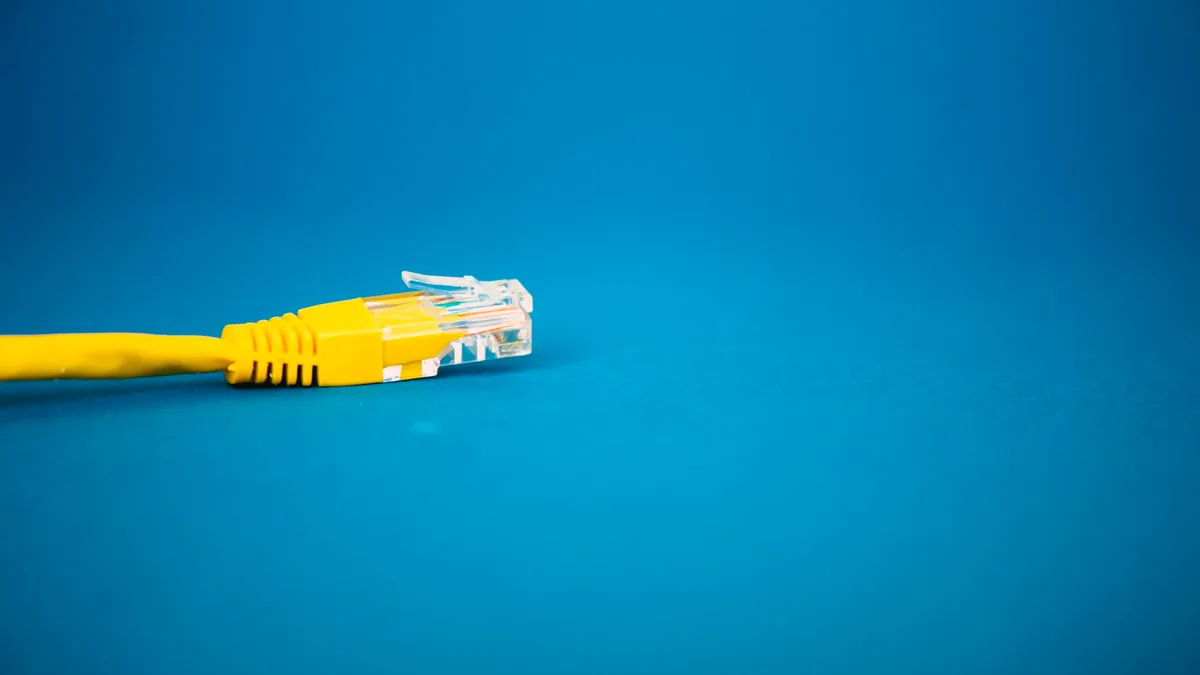 Gelber Netzwerkstecker (Ethernet) in Nahaufnahme vor blauem Hintergrund