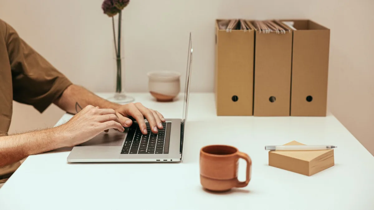 Hände tippen auf einem Laptop an einem aufgeräumten Schreibtisch mit Ordnern